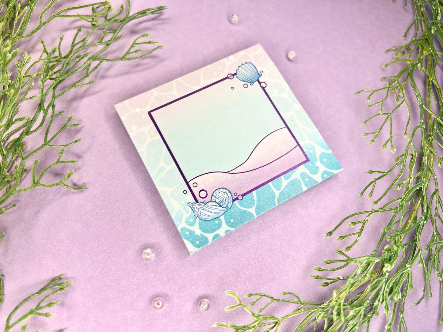A blue and purple sticky note with ocean water around the border, beach in the middle, and shells on the corners of a centered purple square.