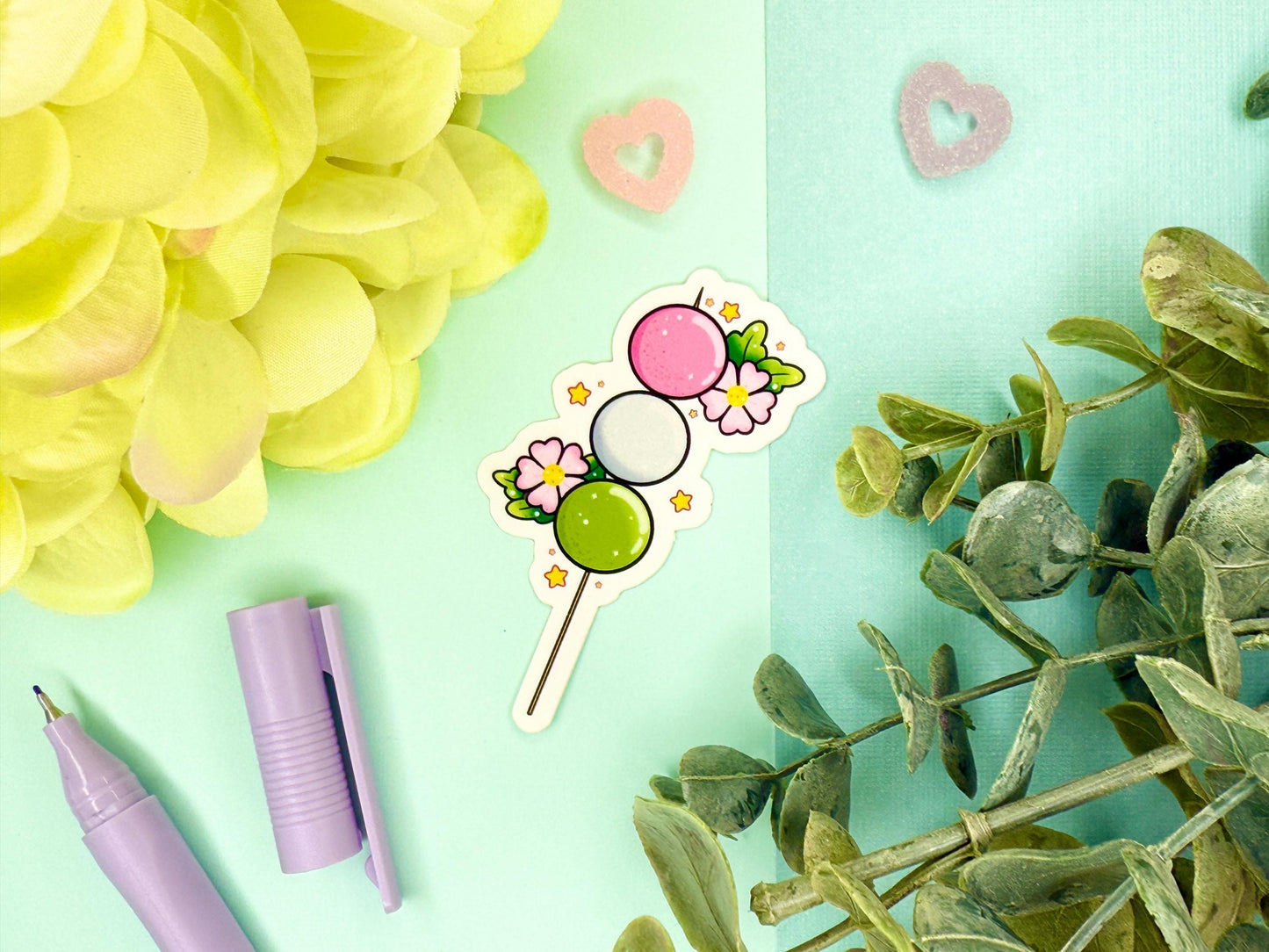Pink, white, and green dango mochi on a stick with pink blossoms around it.