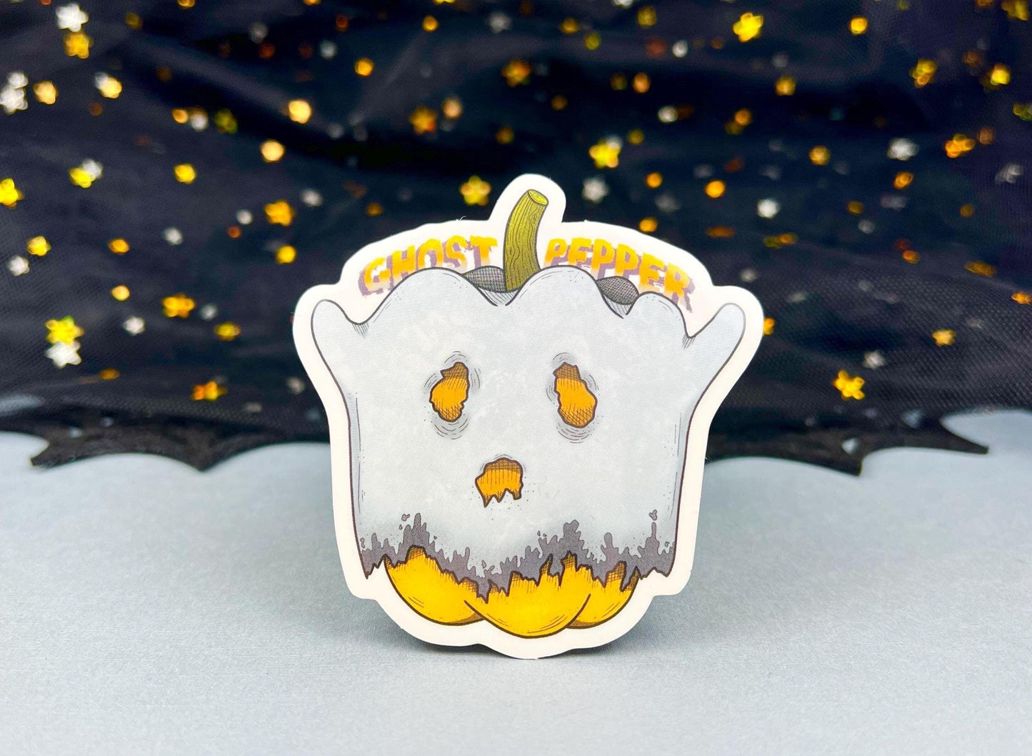 An orange bell pepper sticker with a whitish gray ghost sheet over them and the words Ghost Pepper behind them.