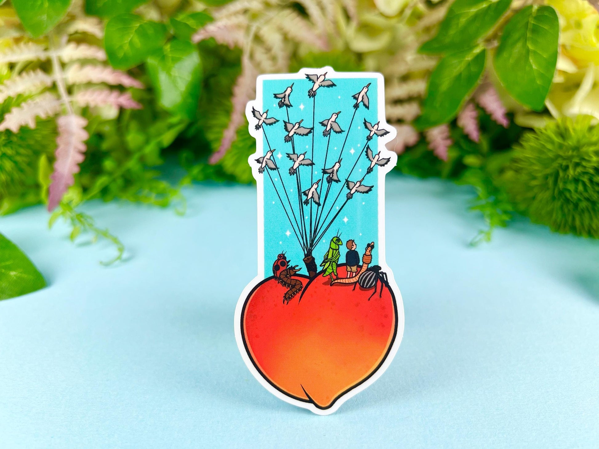 Sticker of a giant peach with people and bugs being carried by birds on a colorful blue background.