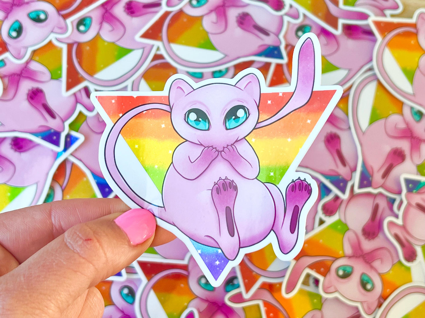 Cute pink cat like creature with blue eyes and an upside-down rainbow striped triangle behind them.