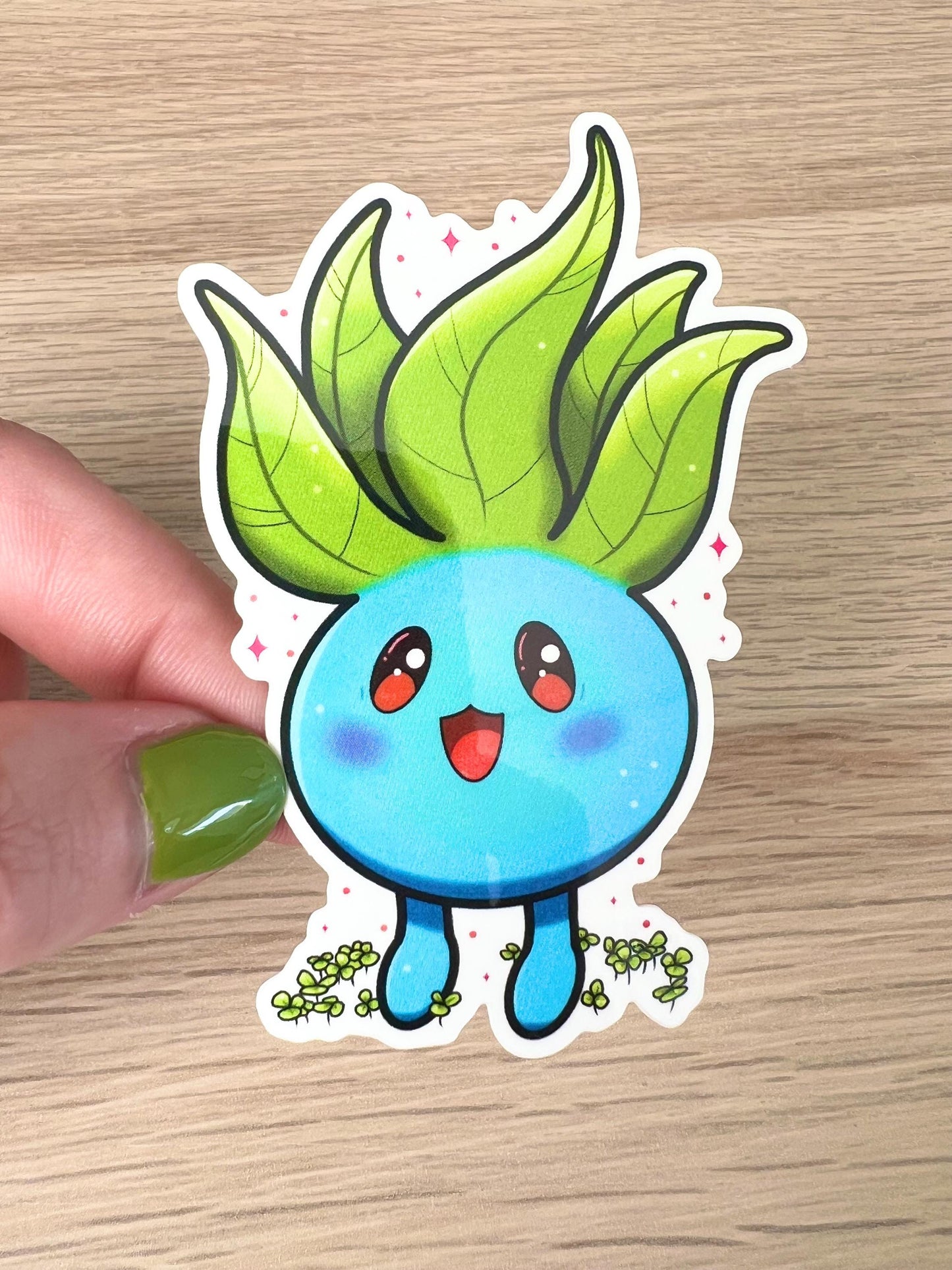 A sticker of a cute blue plant creature with green leaves on top of their head and clovers around their feet.