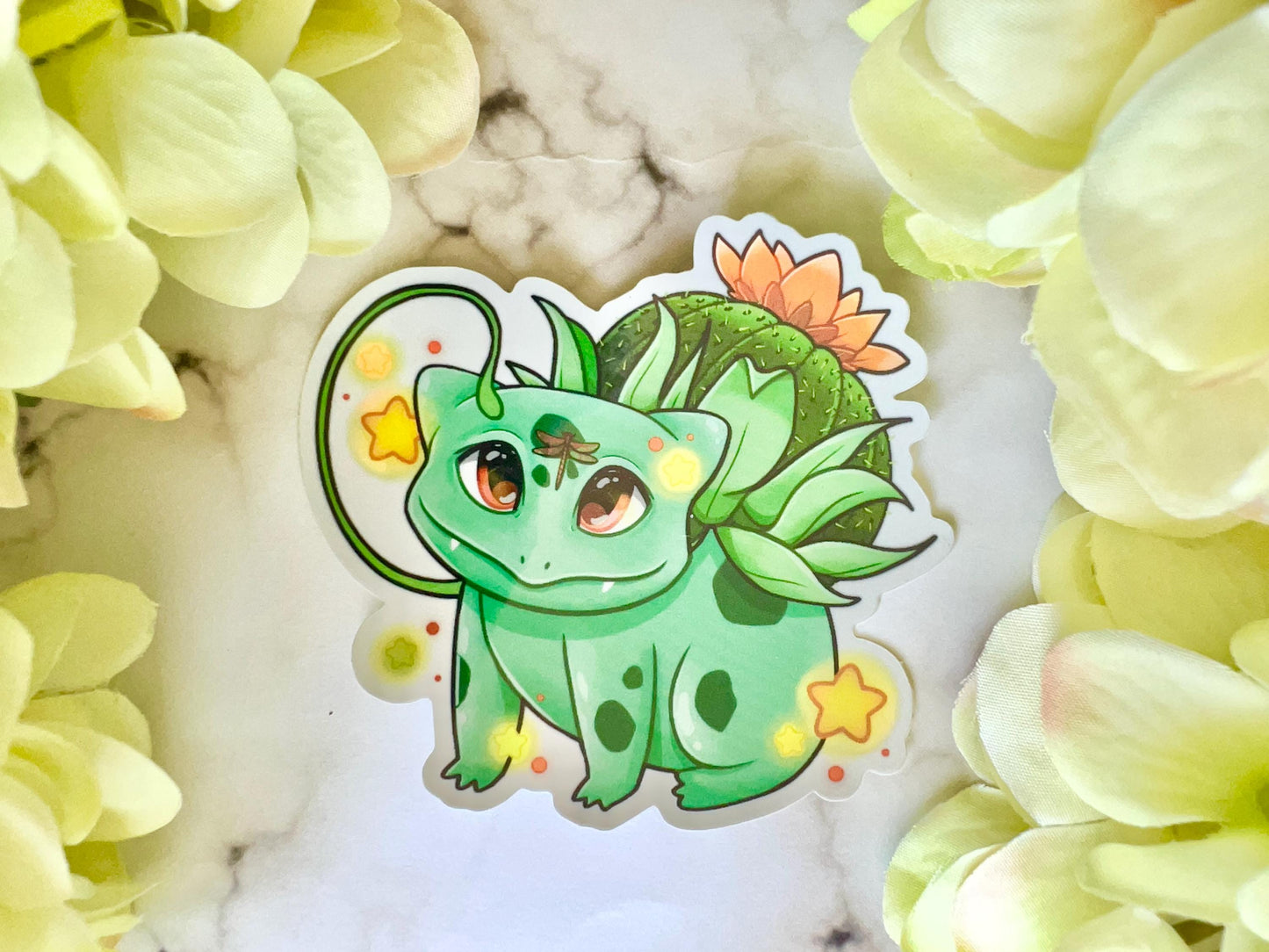 A sticker of a cute 4 legged green plant creature with a cactus and orange flower on its back, vines coming out their side , and yellow glowing stars surrounding them.