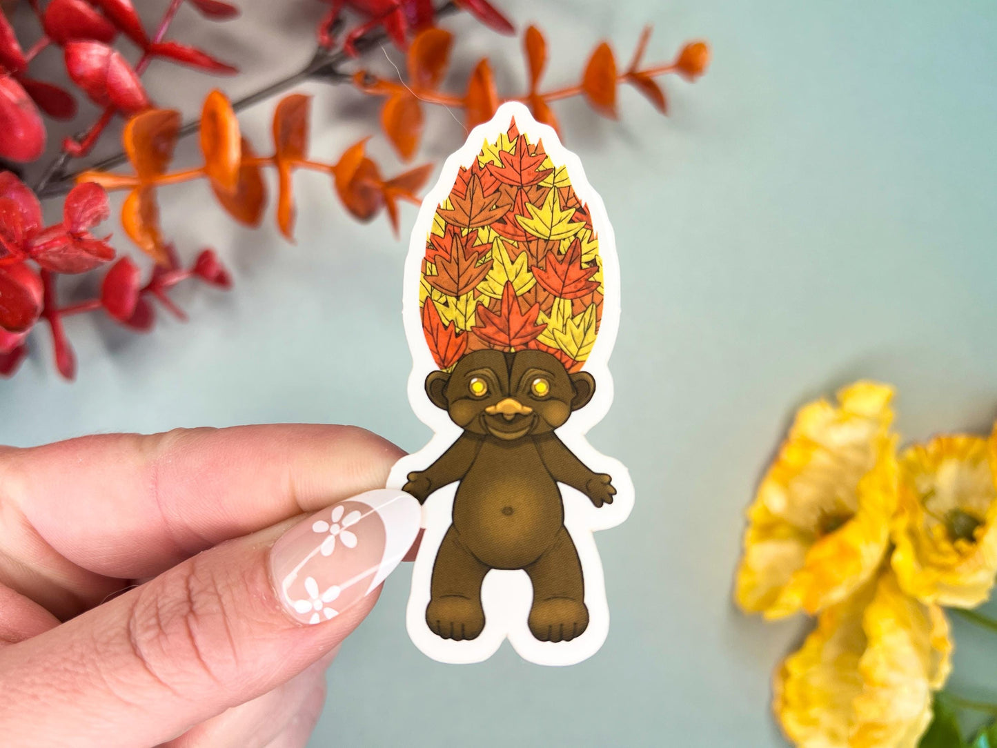 Retro Hair Creature sticker sitting in a pile of orange autumn leaves, about 3 inches tall.
