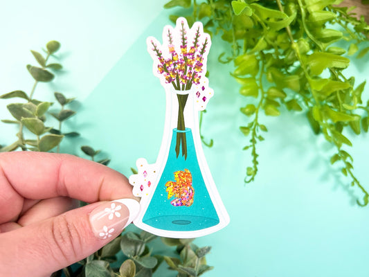 A vase filled with pink and yellow glitter Snapdragon flowers and has water with a pink, orange, and yellow glitter Betta fish inside.