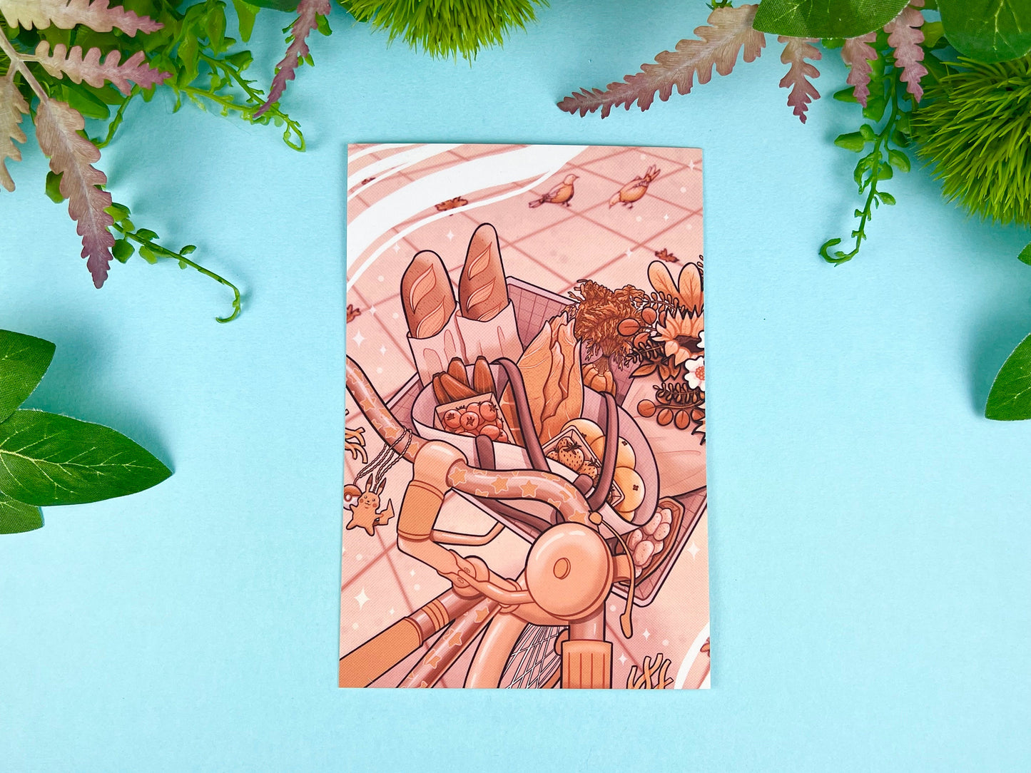 Illustrated postcard with close up of a basket full of groceries on a bicycle with pigeons in the background. 