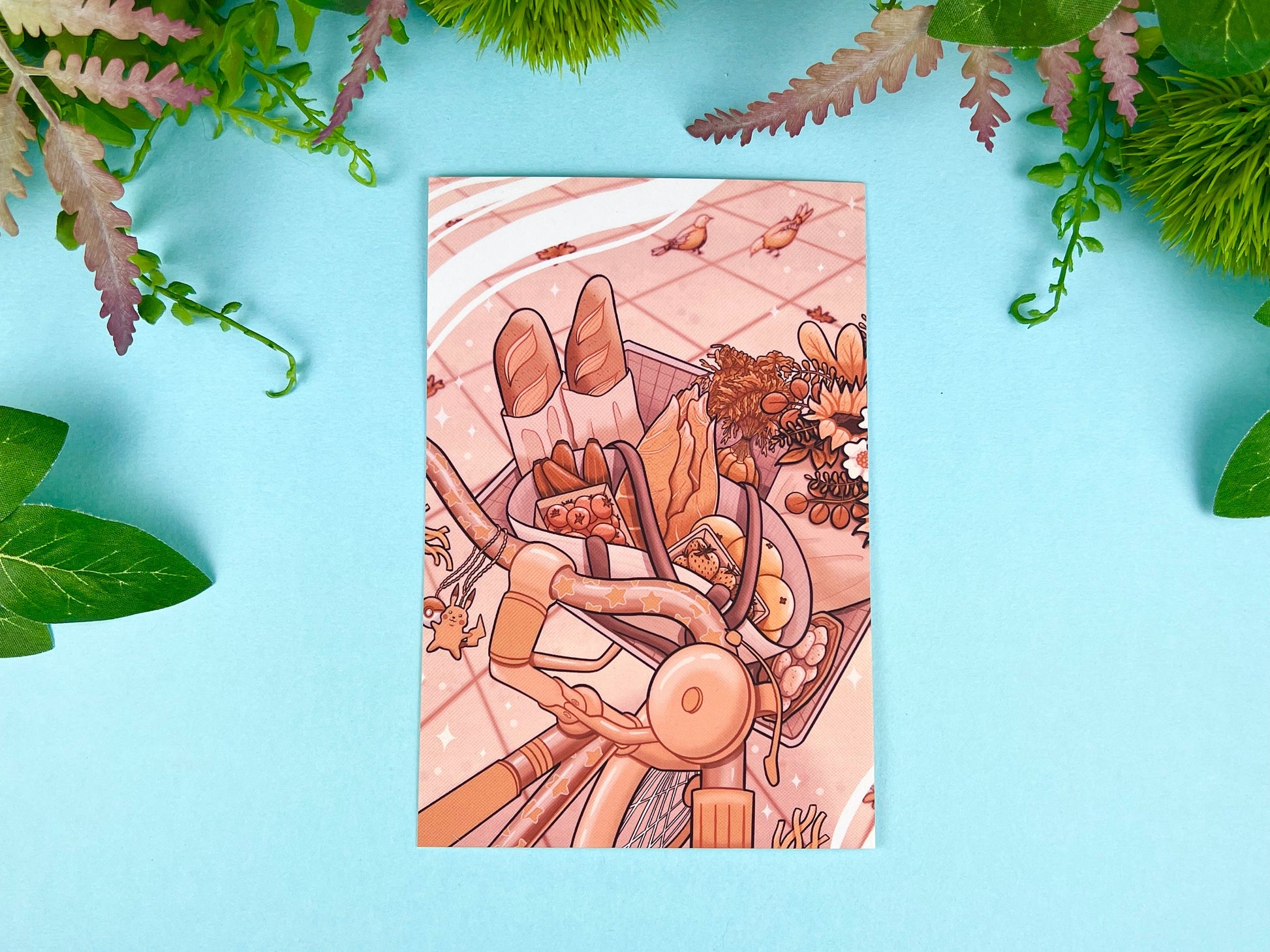 Illustrated postcard with close up of a basket full of groceries on a bicycle with pigeons in the background. 