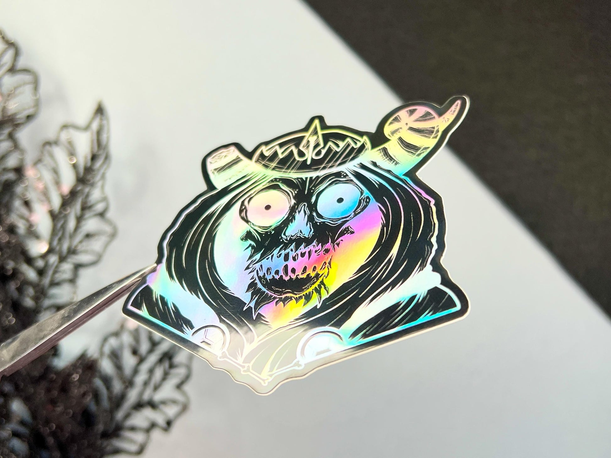 A black and silver holographic sticker of a skull with horns, a crown, a hood, and cape.