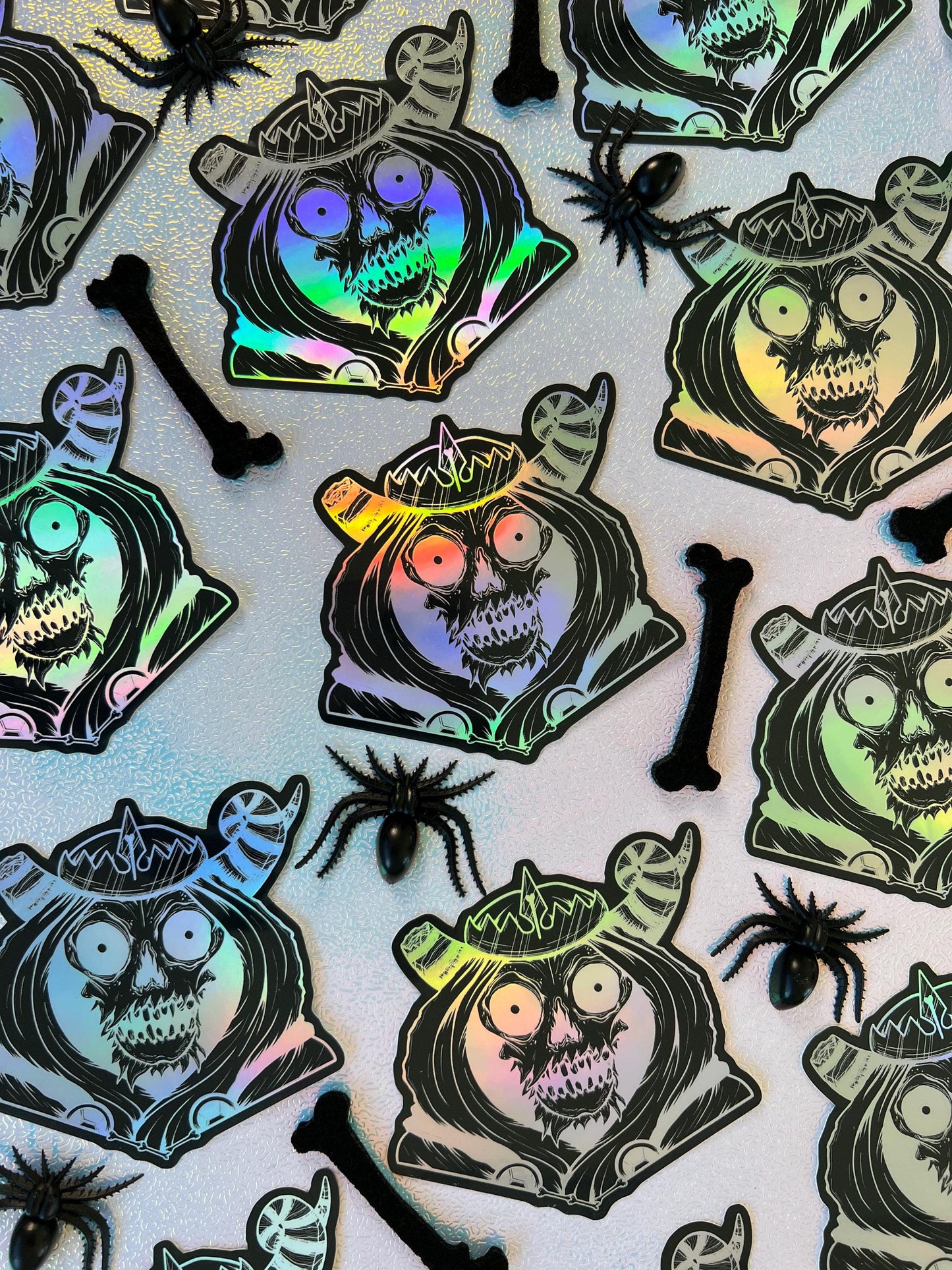 A black and silver holographic sticker of a skull with horns, a crown, a hood, and cape.