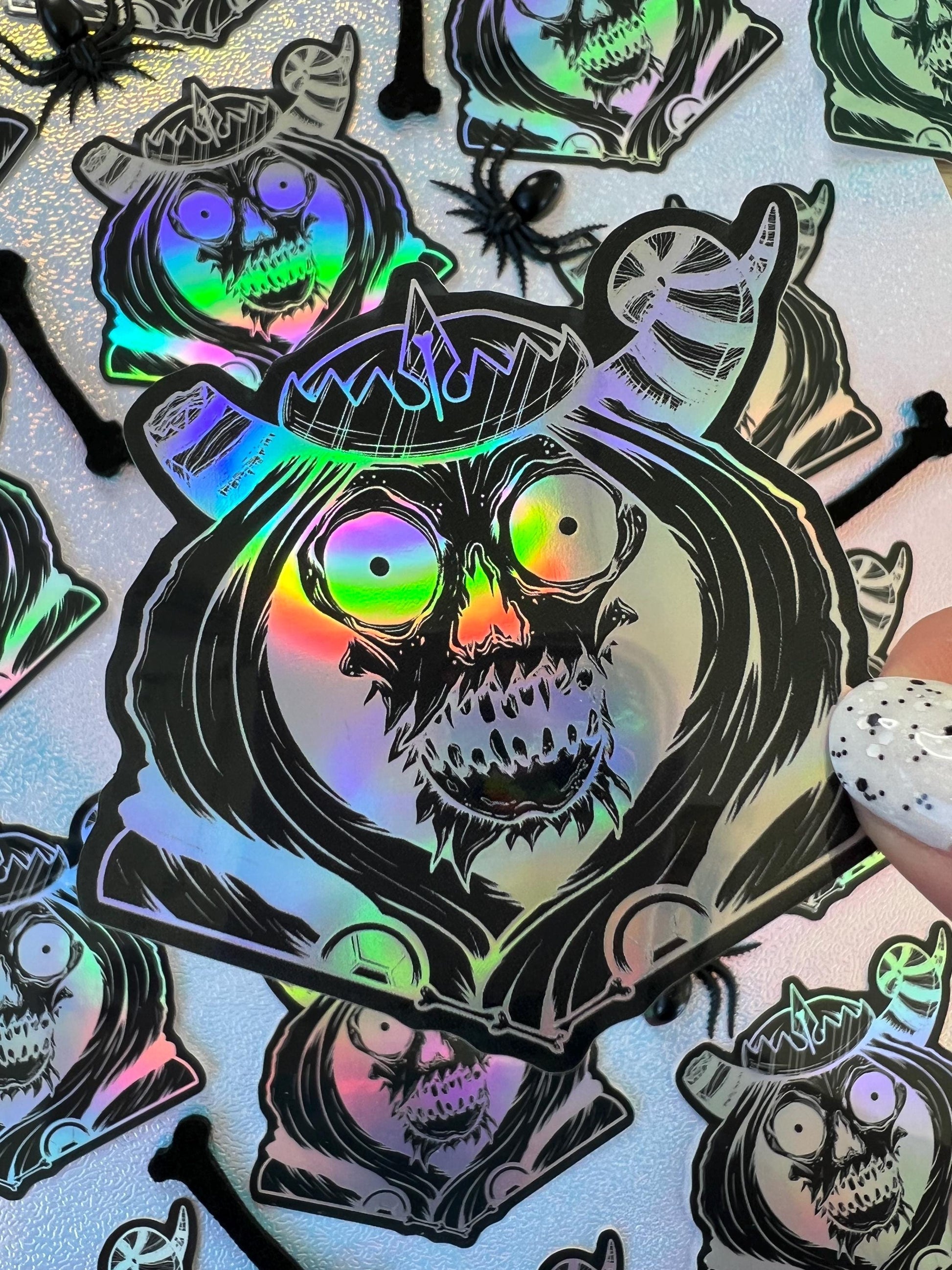 A black and silver holographic sticker of a skull with horns, a crown, a hood, and cape.