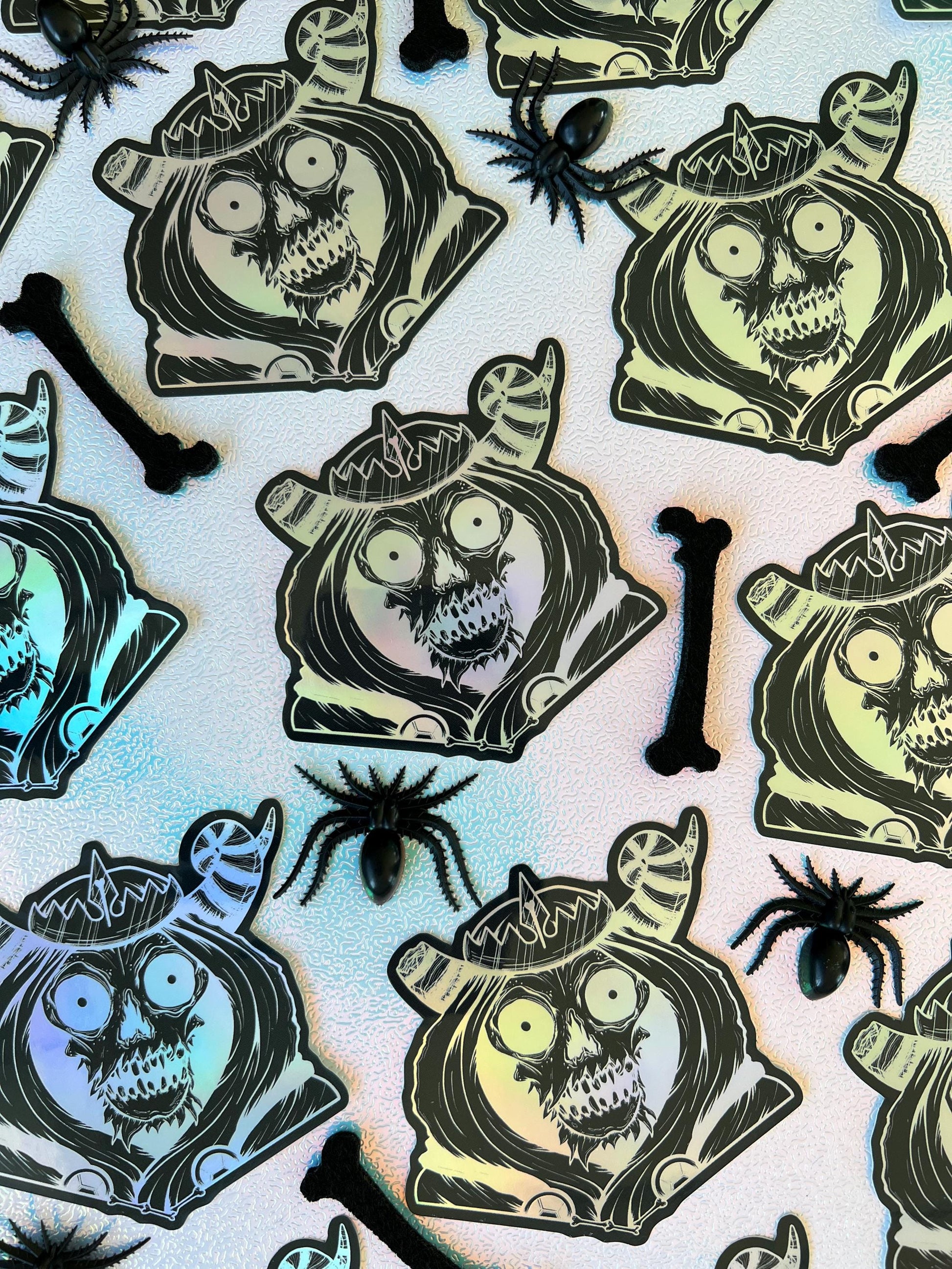 A black and silver holographic sticker of a skull with horns, a crown, a hood, and cape.