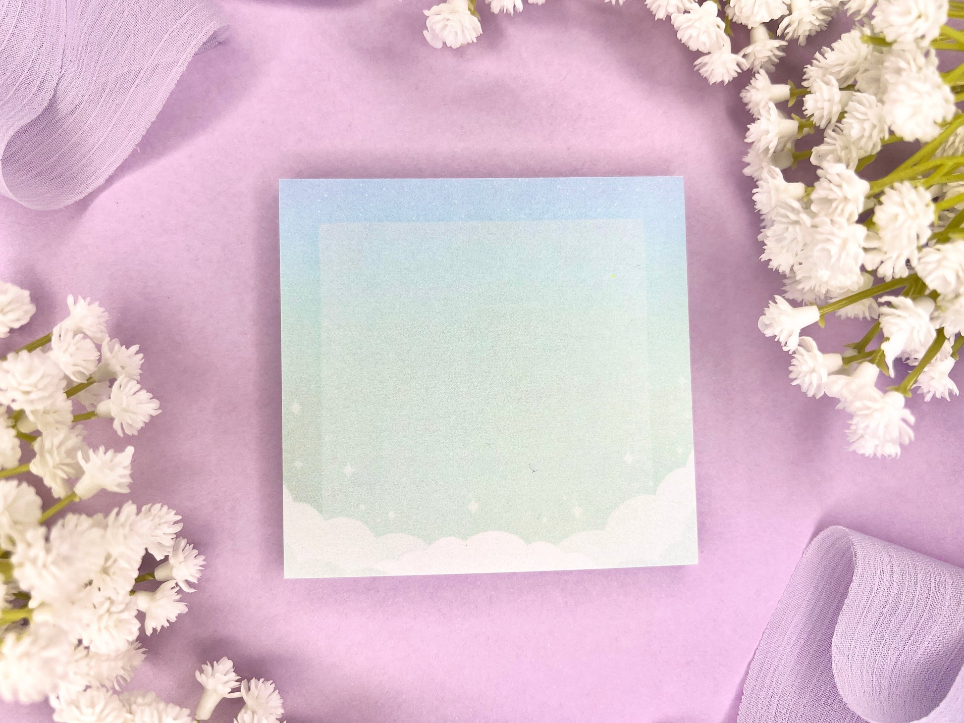 Blue and green sticky notes with clouds bordering the bottom, a faded white square in the middle, and faded sparkles above the clouds.