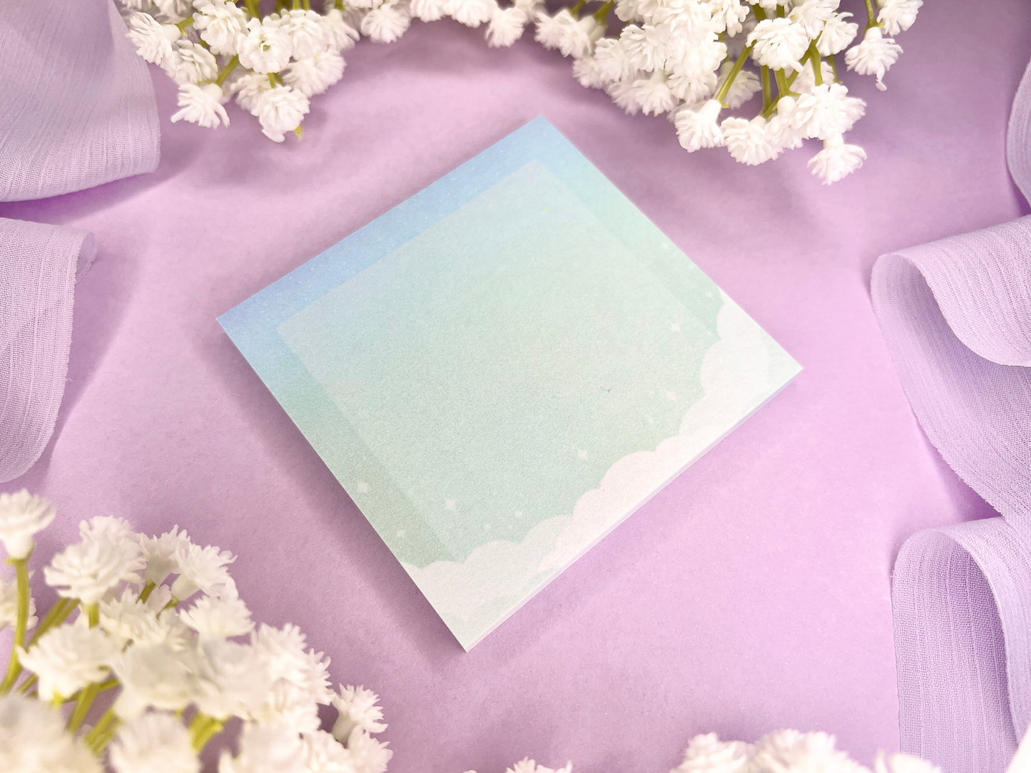 Blue and green sticky notes with clouds bordering the bottom, a faded white square in the middle, and faded sparkles above the clouds.