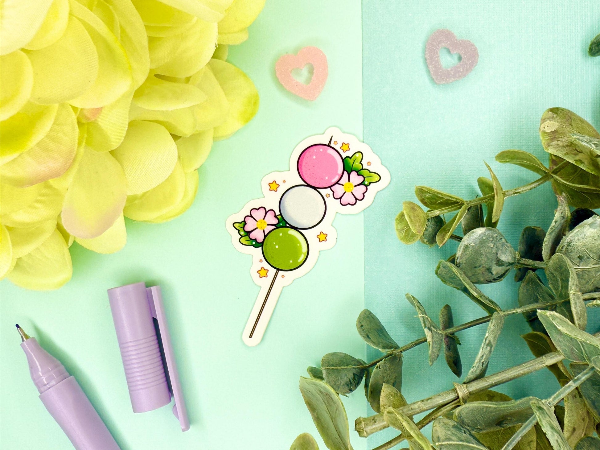 Pink, white, and green dango mochi on a stick with pink blossoms around it.