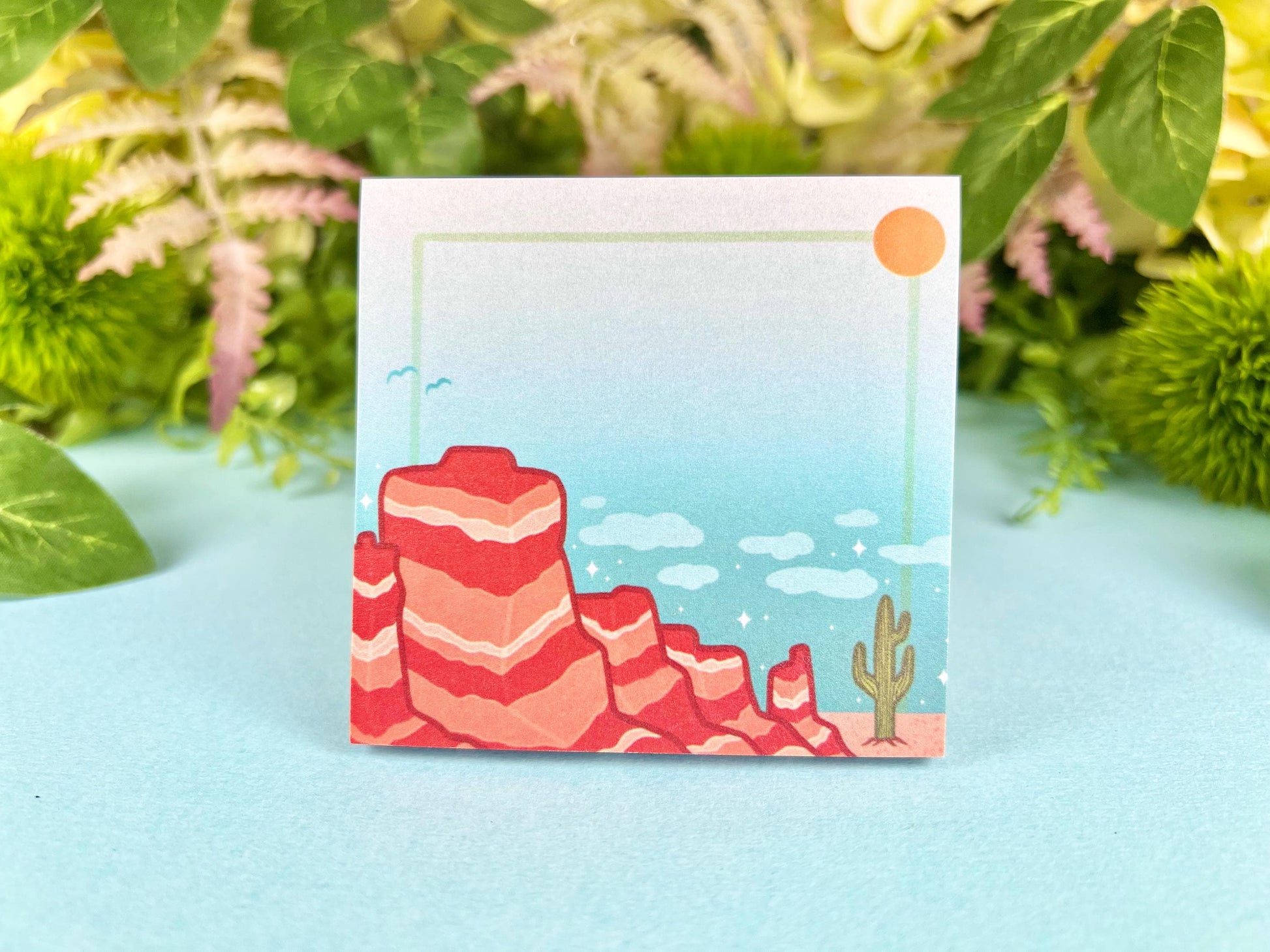 Sticky notes with an illustration of a desert scene with red mountains, a cactus, blue sky, and clouds.