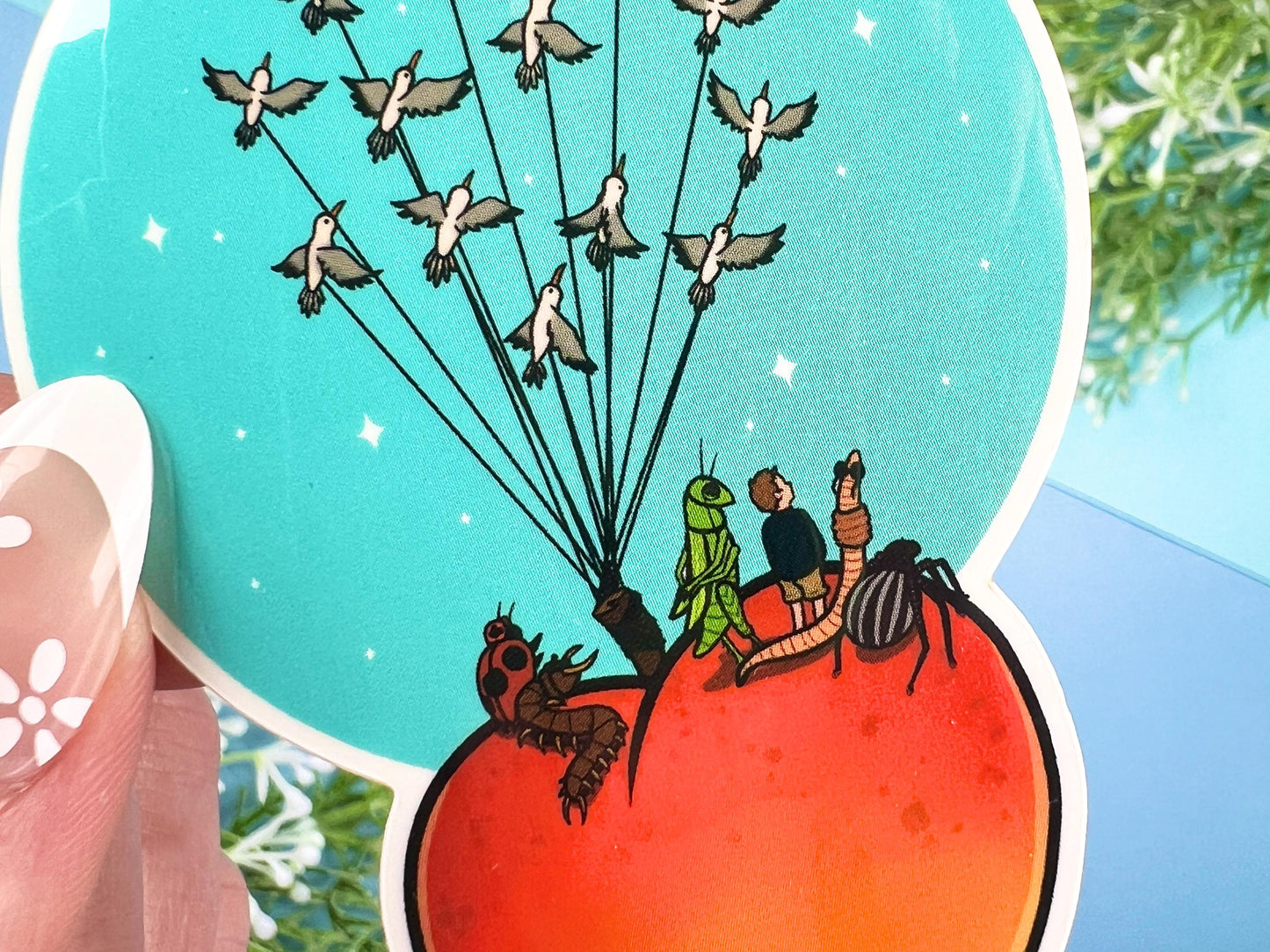 Sticker of a giant peach with people and bugs being carried by birds on a colorful blue background.