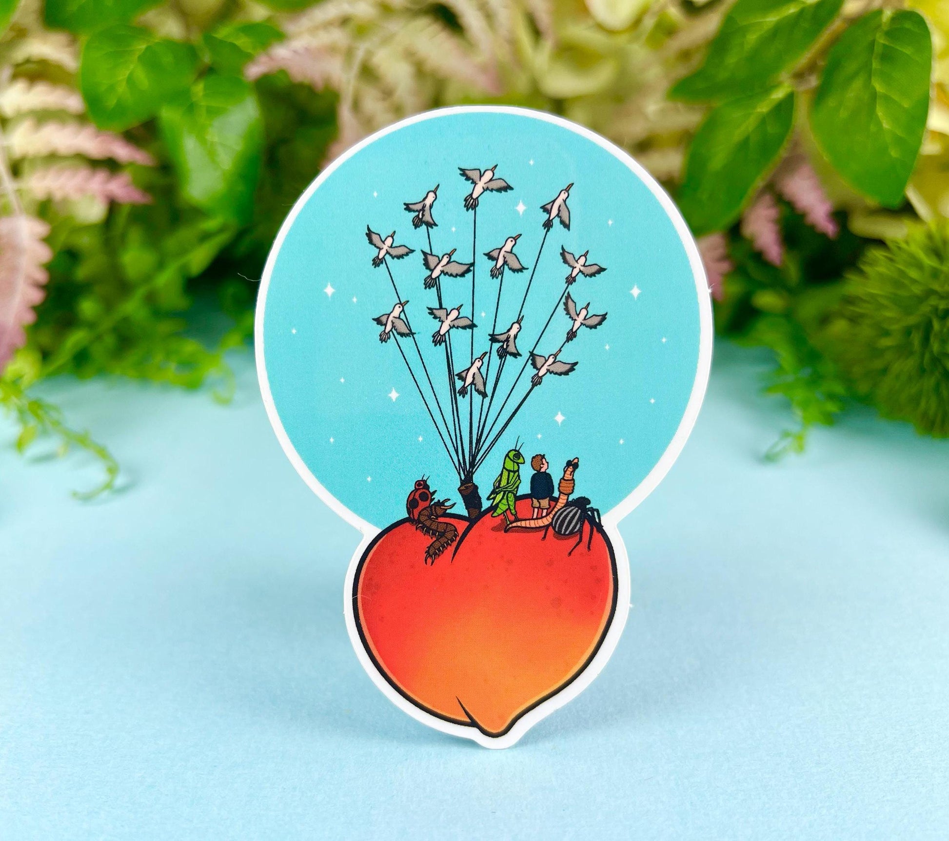 Sticker of a giant peach with people and bugs being carried by birds on a colorful blue background.