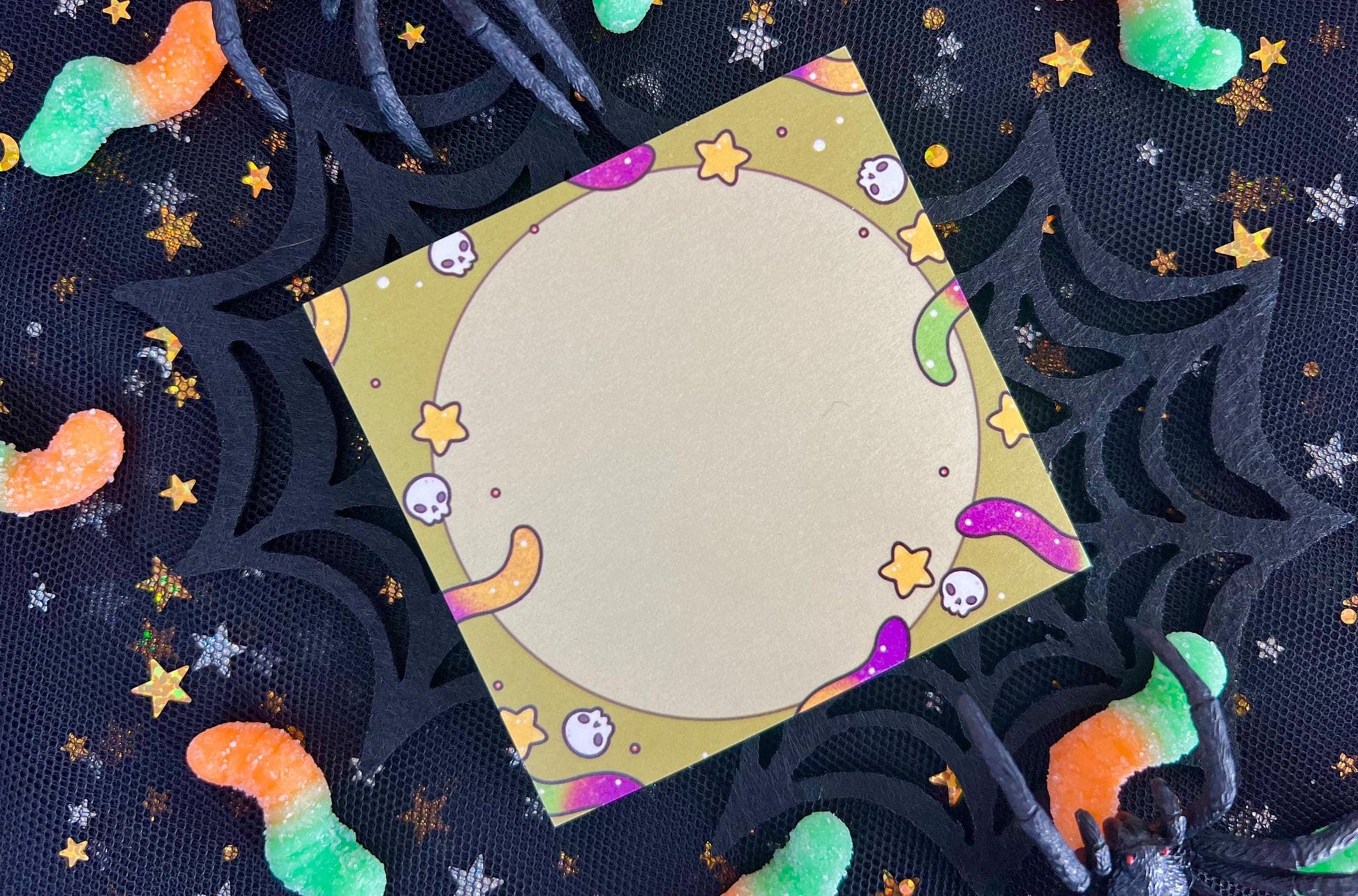 Green background sticky notes with purple and yellow and purple and green gummy worms, skulls, and yellow stars surrounding a circle in the middle.