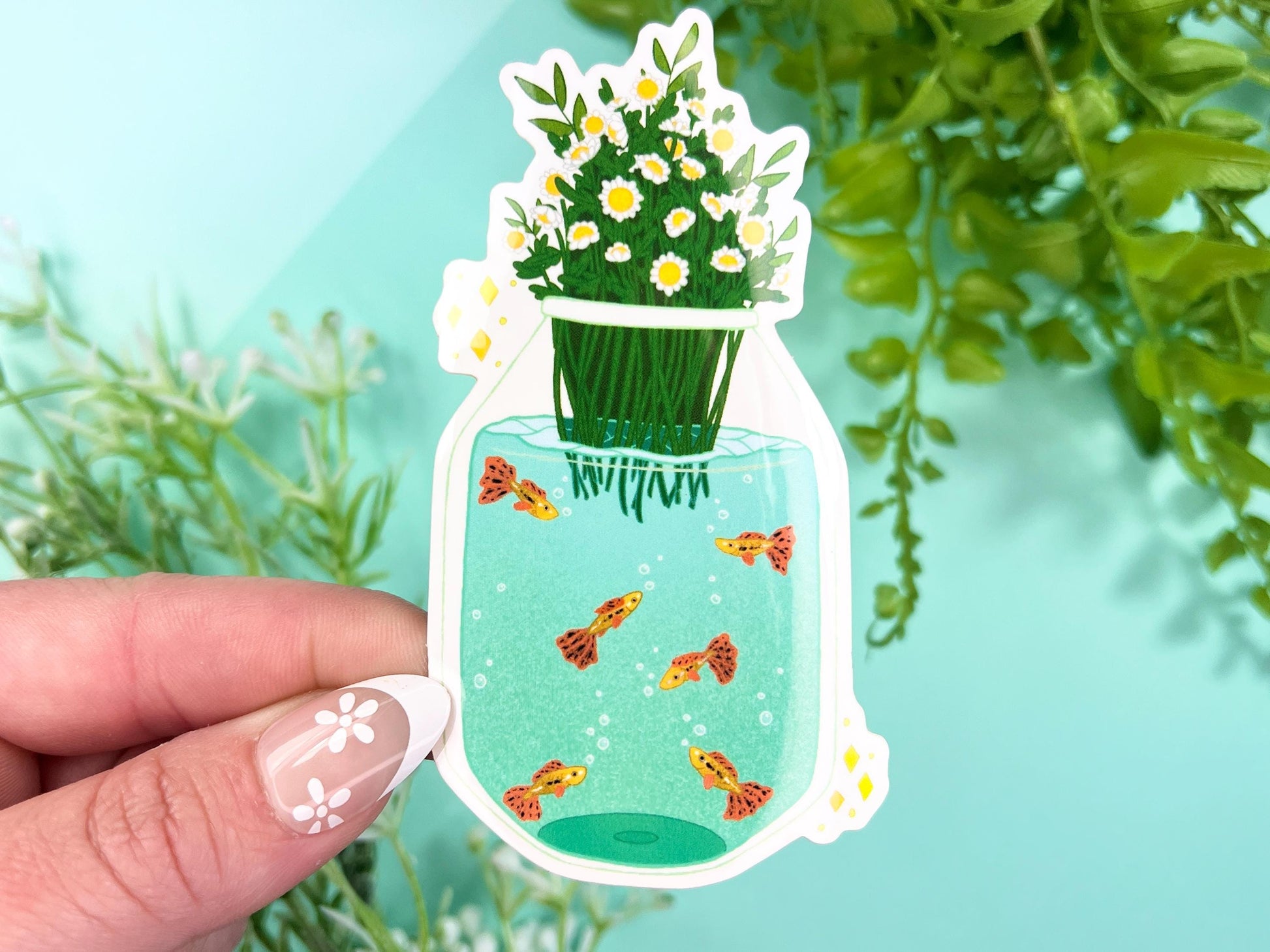 A vase filled with white and yellow chamomile flowers and has water with orange, yellow, and black spotted Guppy fish inside.