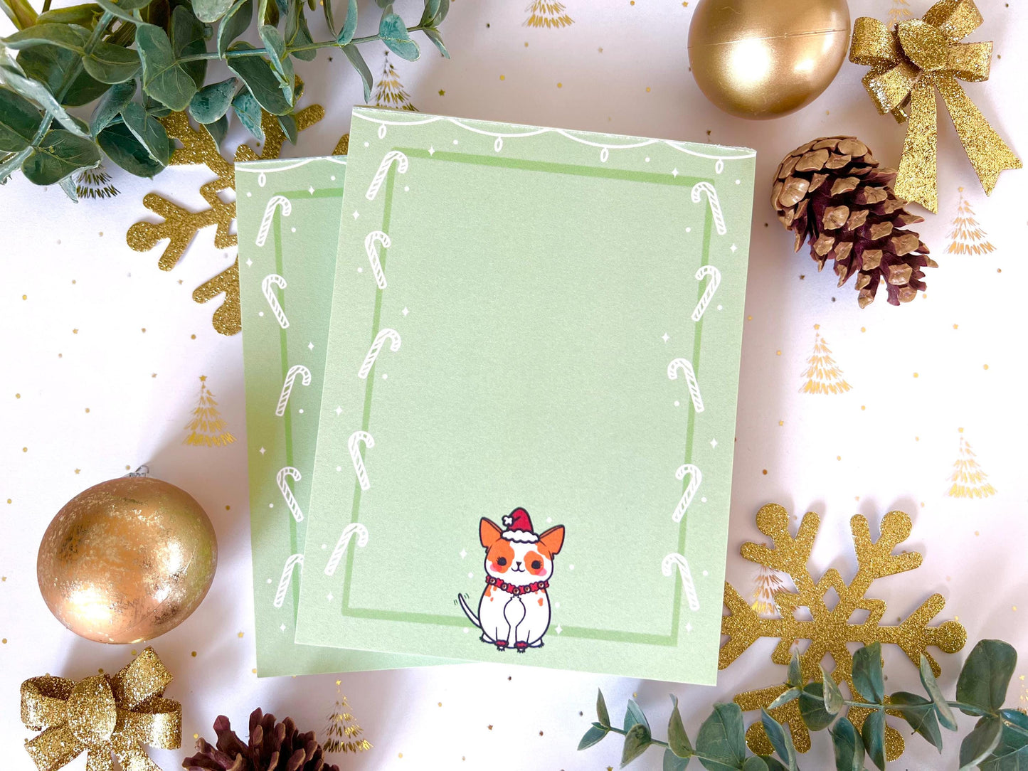 A green notepad that has an illustration of a cute dog dressed up in a Santa hat and bells and has a green and white candy cane border around it.