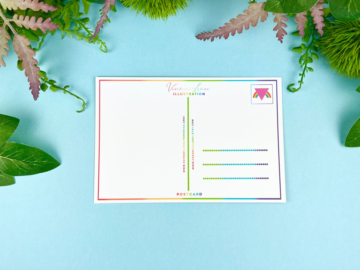 Back of the postcard with a line down the middle, lines on the right side for and address, and a cute LGBTQIA+ pink triangle rainbow illustration where the stamp would go. 