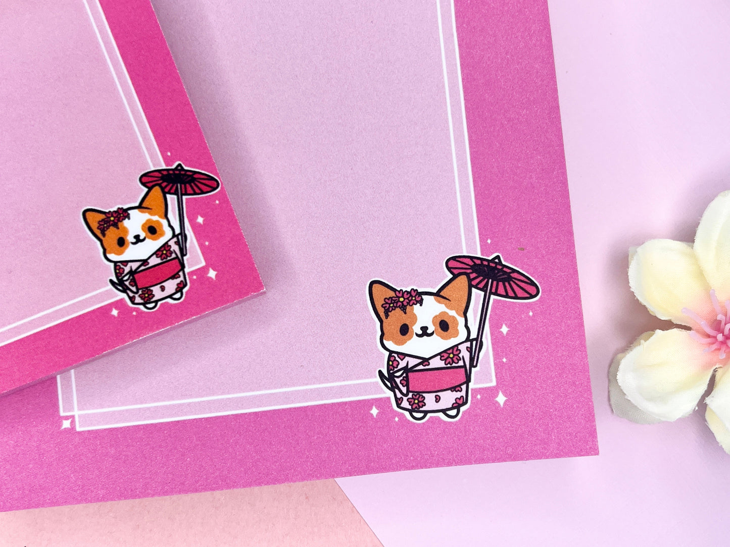 A pink gift set, including sticky notes and a notepad, that has an illustration of a cute dog wearing a pink kimono holding an umbrella under cherry blossoms. 
