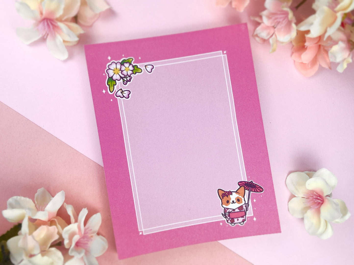 A pink notepad that has an illustration of a cute dog wearing a pink kimono holding an umbrella under cherry blossoms. 