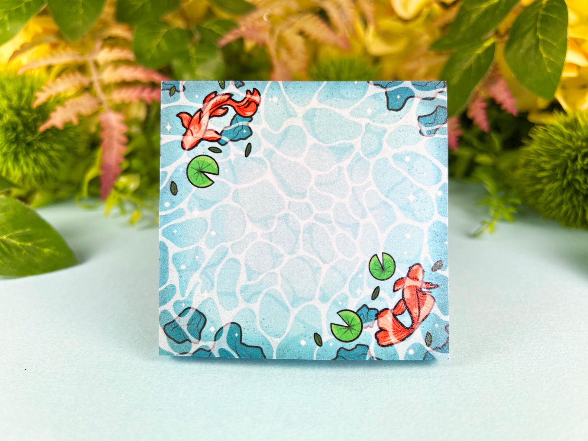Blue sticky notes of water from a pond with rocks, green lily pads, and orange koi swimming around.
