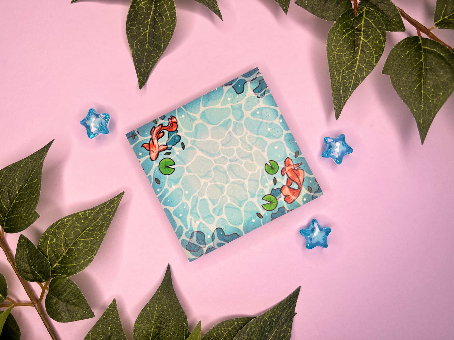 Blue sticky notes of water from a pond with rocks, green lily pads, and orange koi swimming around.