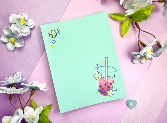 Light blue notepad with an illustration of pink boba milk tea surrounded by pink flowers.