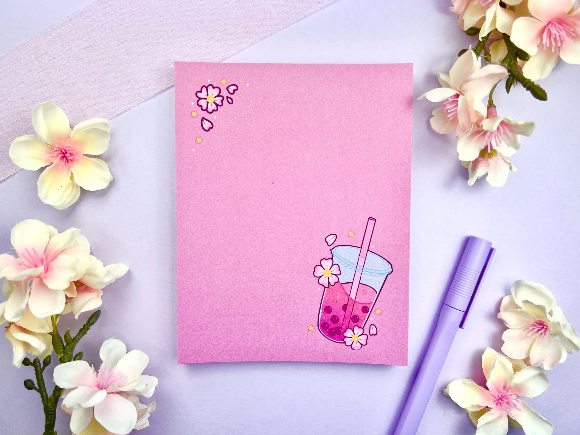 Pink notepad with a pink boba milk tea illustration surrounded by pink flowers and yellow stars.
