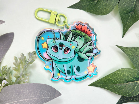 A keychain of a cute 4 legged green plant creature with a cactus and orange flower on its back, vines coming out their side , and yellow glowing stars surrounding them.