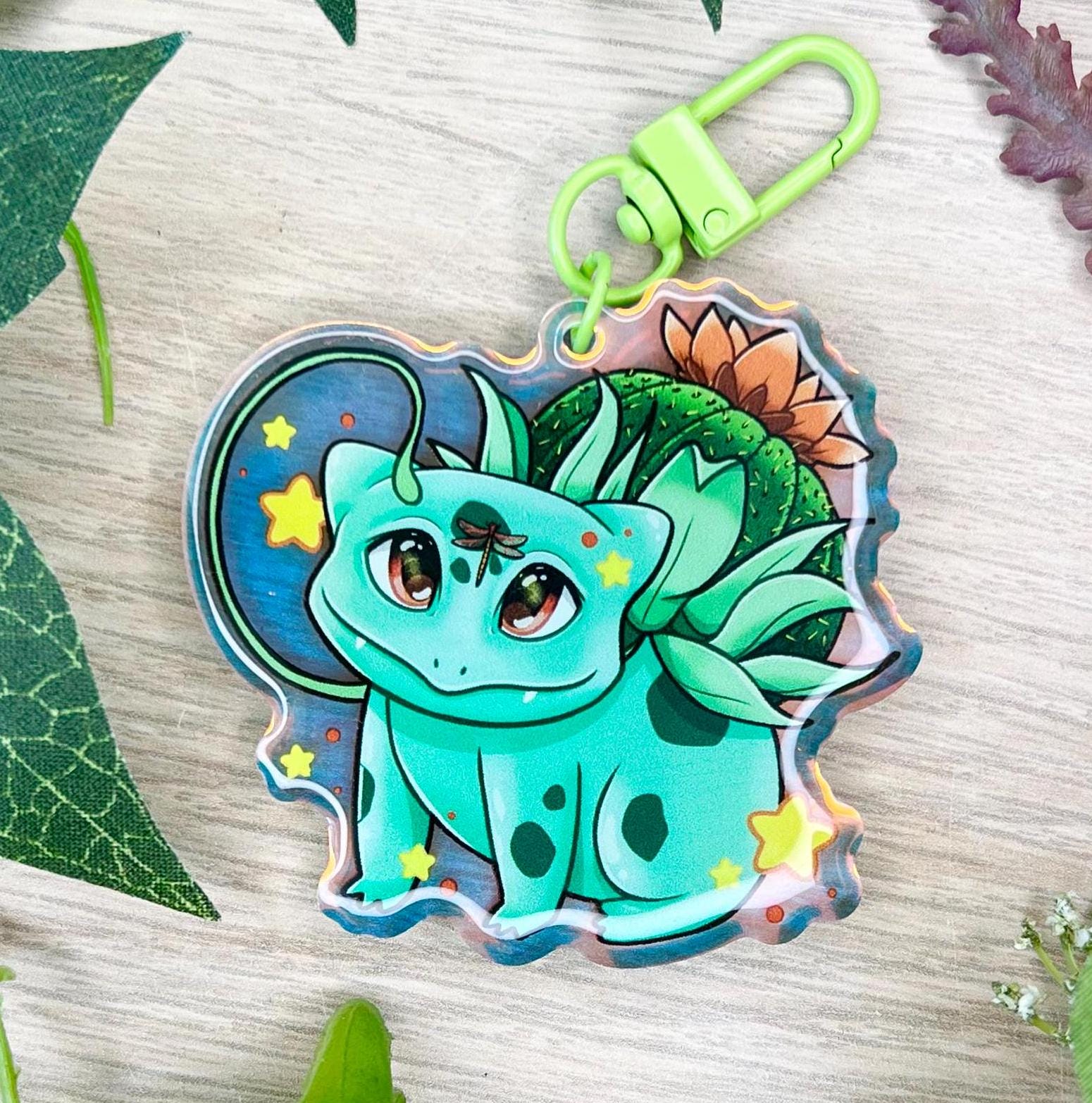A keychain of a cute 4 legged green plant creature with a cactus and orange flower on its back, vines coming out their side , and yellow glowing stars surrounding them.