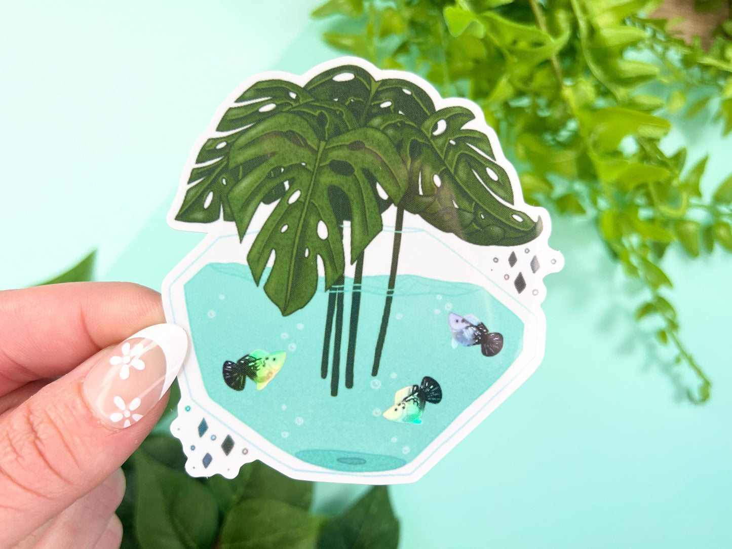 A vase filled with green Monstera leaves and has water with white and black holographic Platy fish inside.