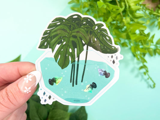 A vase filled with green Monstera leaves and has water with white and black holographic Platy fish inside.