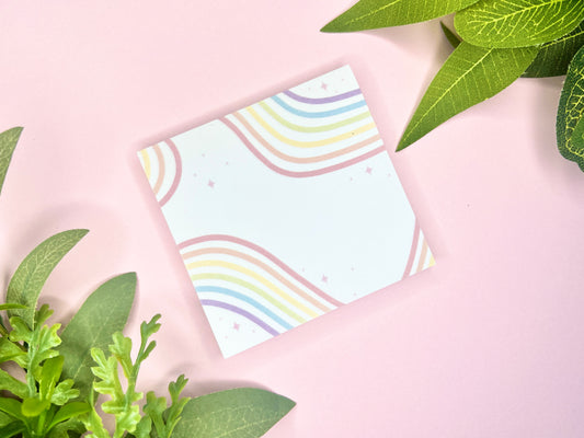 White sticky notes with rainbow ribbons flowing across it and sparkles all around.