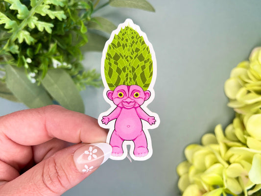 A pink retro hair creature with green hair made to look like tropical leaves.