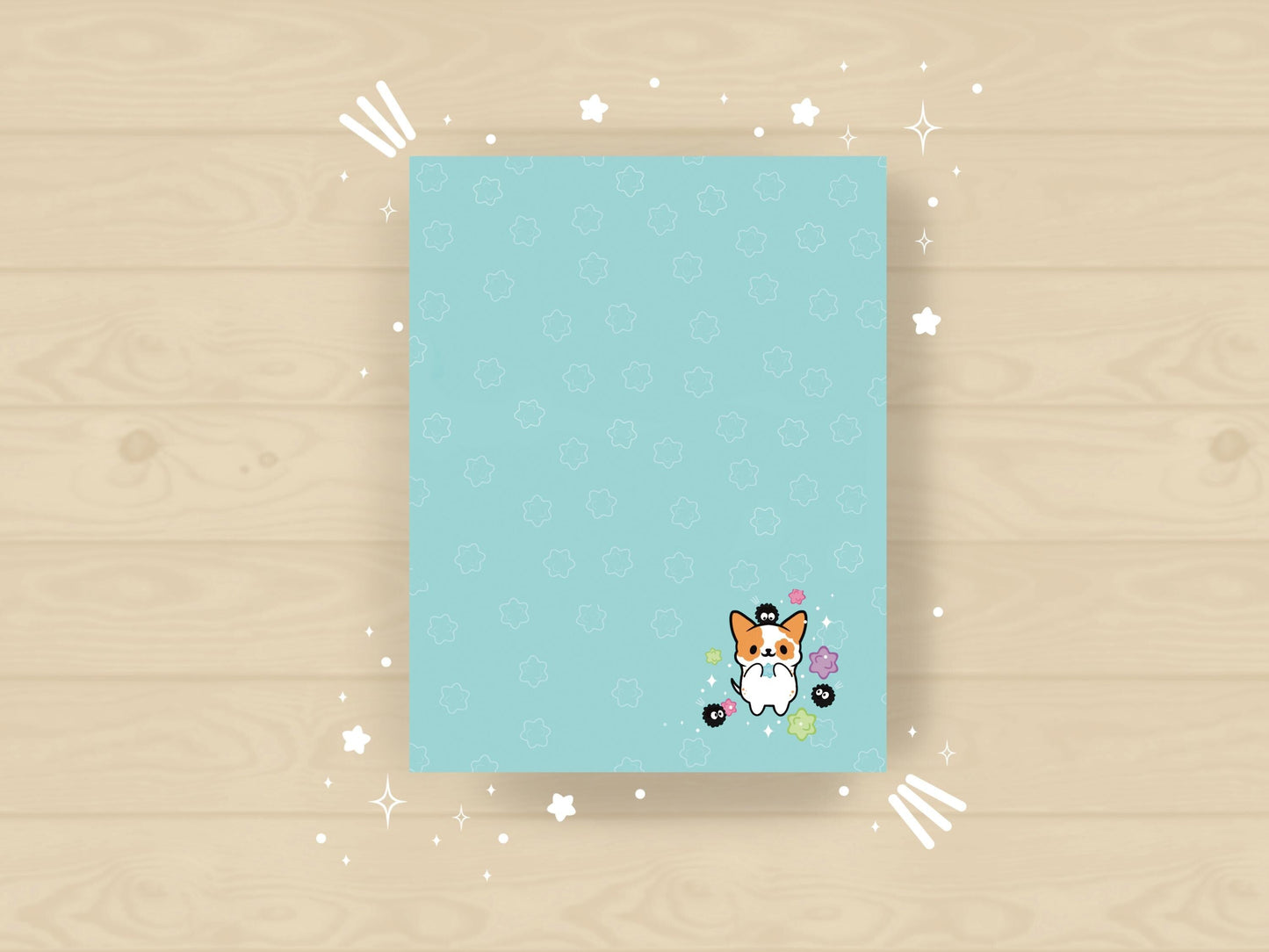 A blue notepad with an illustration of a cute dog playing with soot sprites and rainbow konpieto and has a konpieto patterned background.