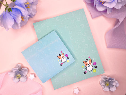 A blue gift set that includes one sticky note pad and one notepad with an illustration of a cute dog playing with soot sprites and rainbow konpieto and has a konpieto patterned background.