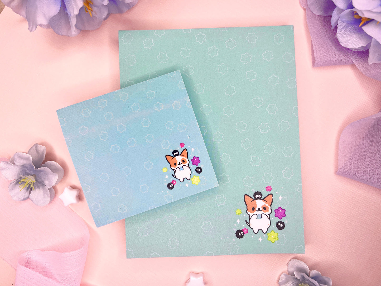 A blue gift set that includes one sticky note pad and one notepad with an illustration of a cute dog playing with soot sprites and rainbow konpieto and has a konpieto patterned background.