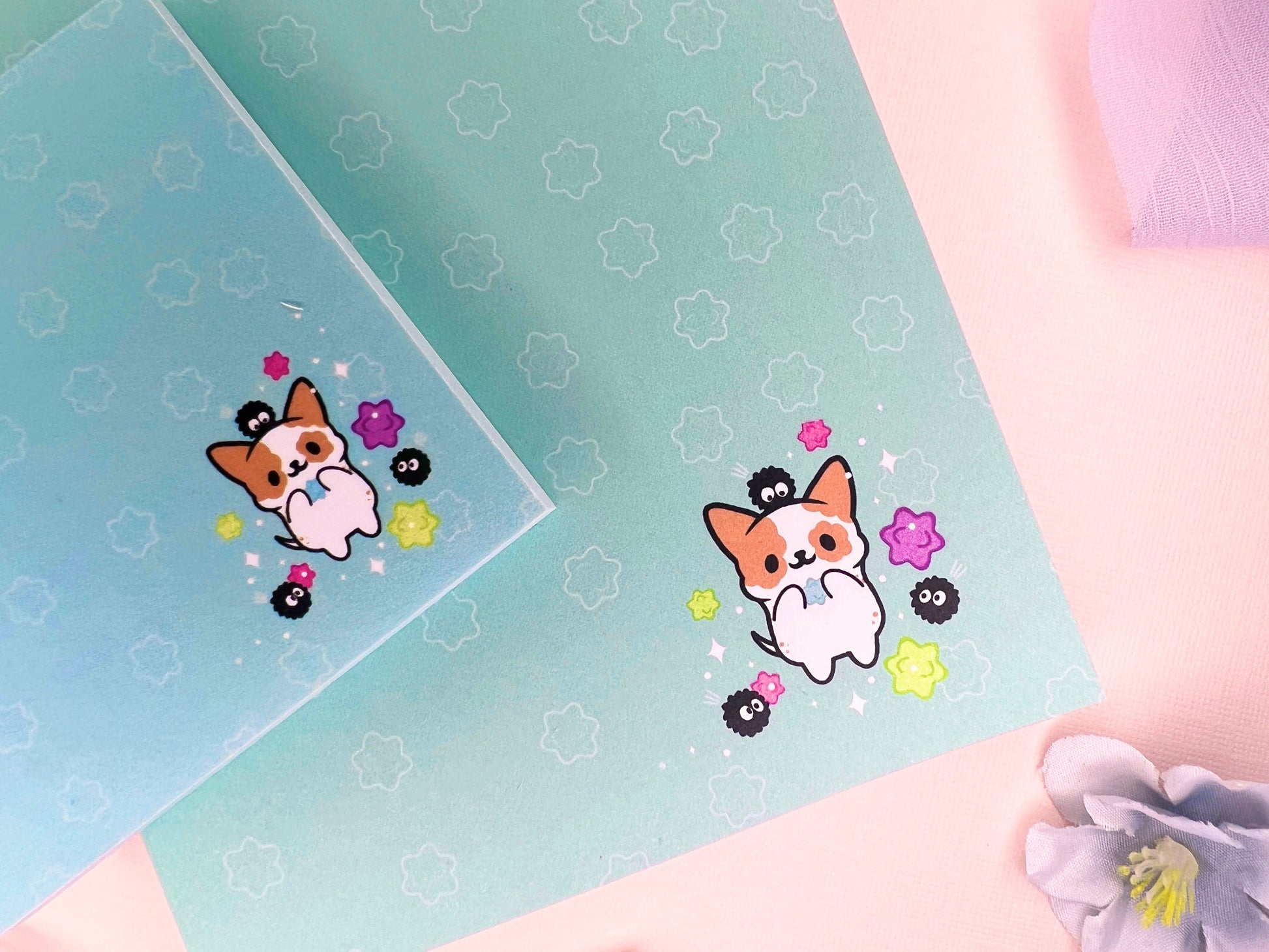 A blue gift set that includes one sticky note pad and one notepad with an illustration of a cute dog playing with soot sprites and rainbow konpieto and has a konpieto patterned background.