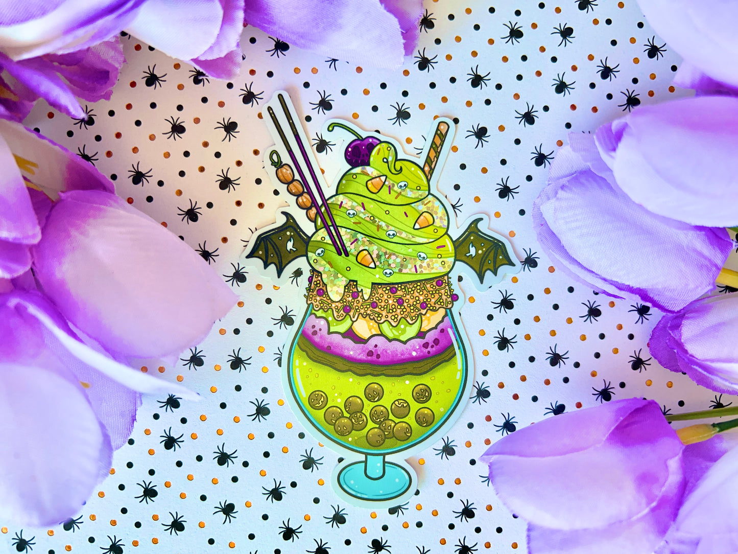 A green, orange, and purple sticker illustration of a spooky drink with jack o'lantern boba, frosting, sprinkles, whip cream, candy corn, a skull cherry, straw and bat wings.