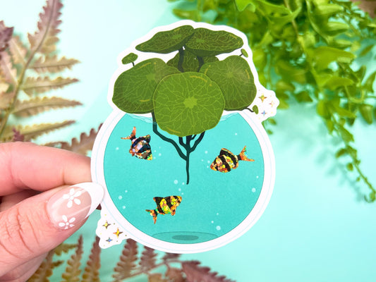 A vase filled with green Pilea leaves and has water with orange and black glitter Tiger Barb fish inside.