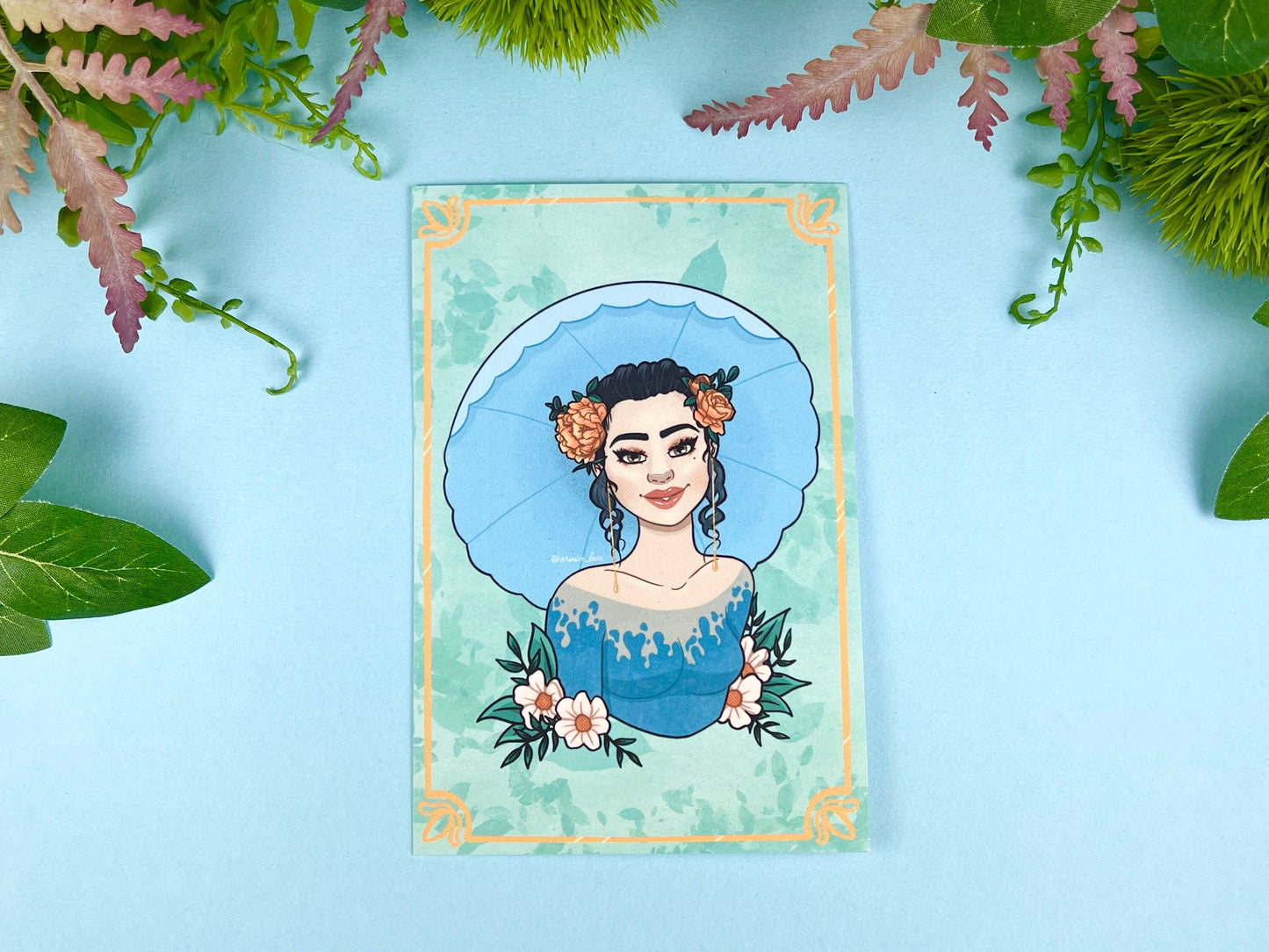 Illustrated card with a woman's portrait holding an umbrella on a blue polka dot background with orange and white flowers.