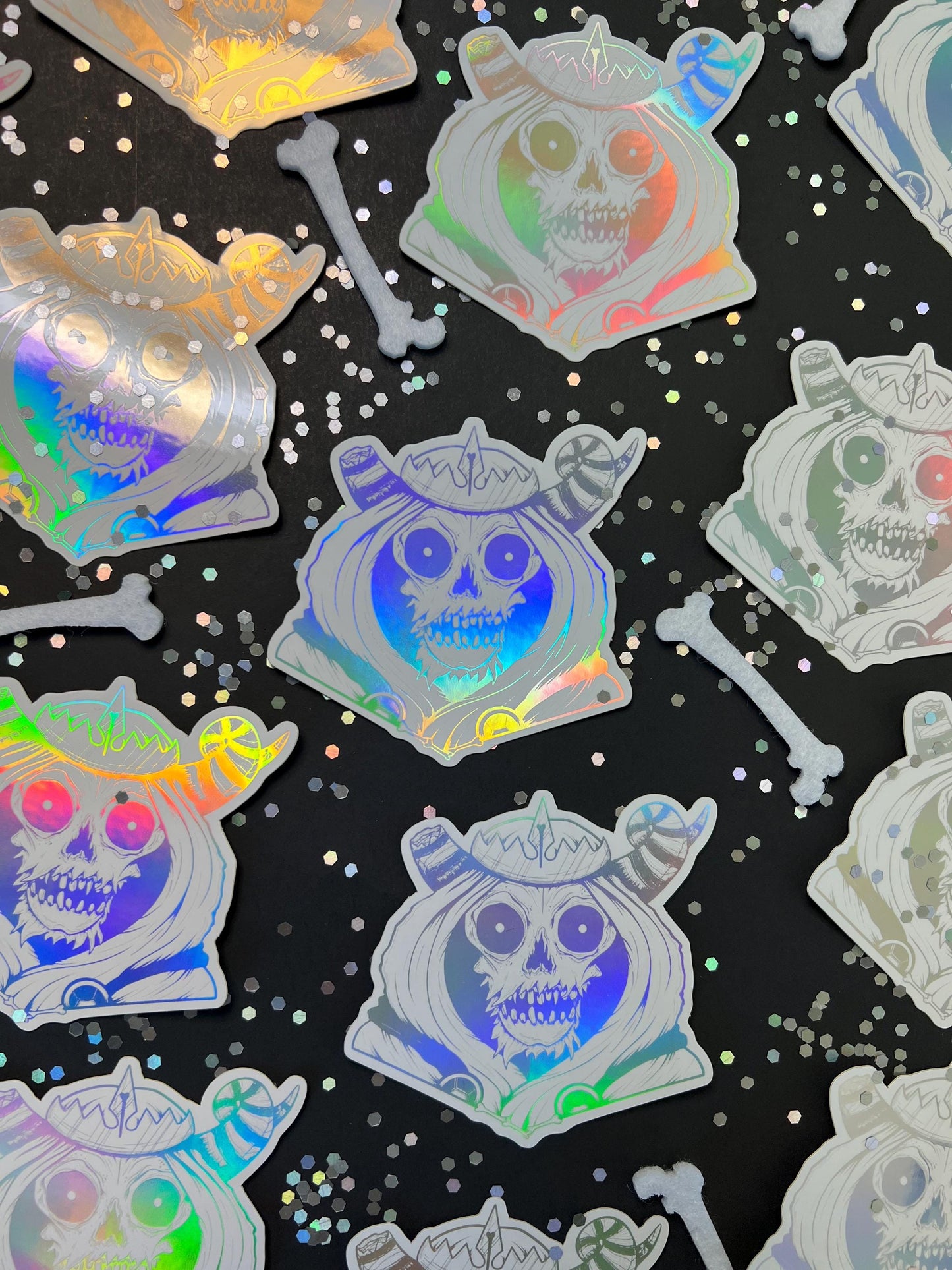 A white and silver holographic sticker of a skull with horns, a crown, a hood, and cape.